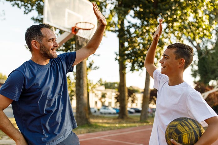 Father and teen son playing basketball high-fiving