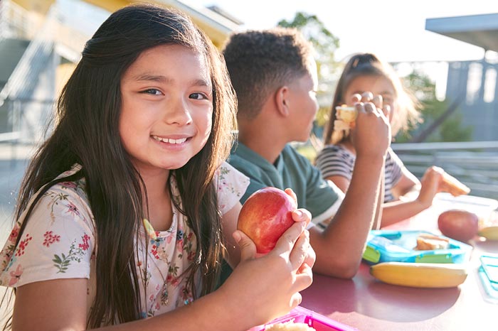 Girl at elementary school lunch table smiling to camera