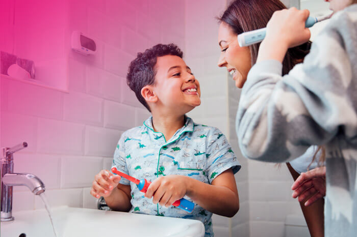 Children are brushing their teeth in the bathroom at home. The mother is checking the little boy's mouth to make sure he has brushed properly.
