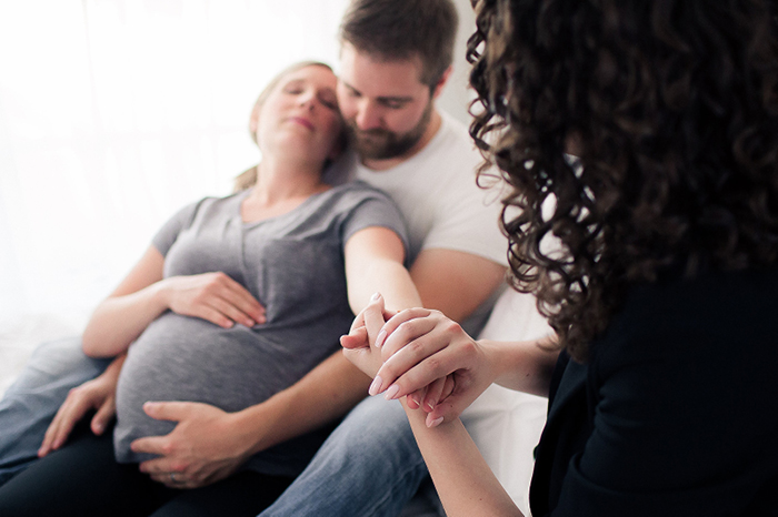 A doula comforting and holding a pregnant woman's hand during labor. Male partner holding pregnant woman during labor.