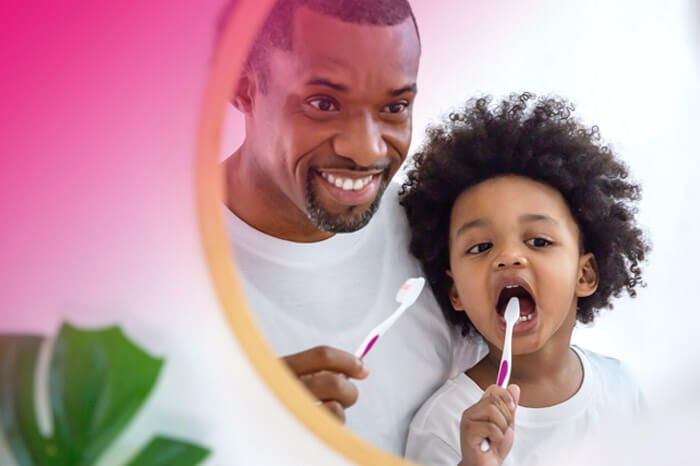 father and young daughter looking in a mirror brushing their teeth