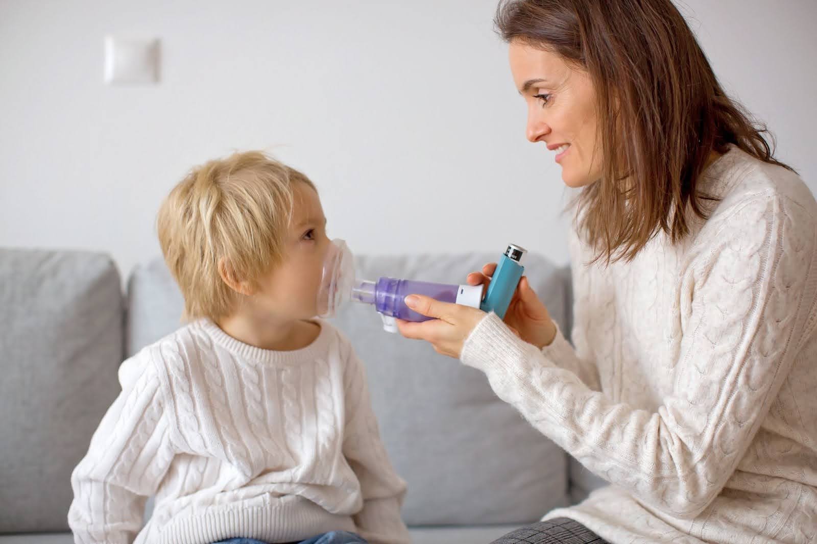Mother helping child use inhaler with spacer for asthma treatment